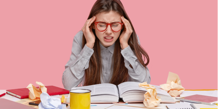 Estudante estressada com dor de cabeça durante sessão de estudos.