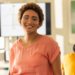 Professora sorridente em sala de aula moderna com estudantes ao fundo.
