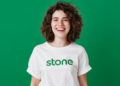 Jovem sorridente com camiseta da Stone em fundo verde.