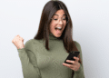 Jovem comemorando novidade no celular com expressão de surpresa.