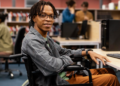 Estudante cadeirante sorrindo em laboratório de informática universitário.