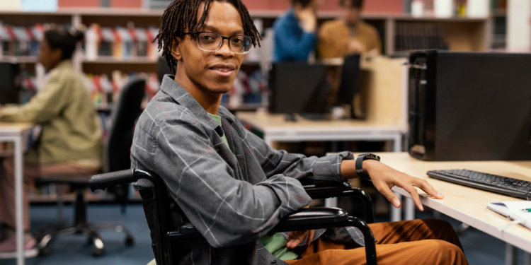 Estudante cadeirante sorrindo em laboratório de informática universitário.