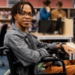Estudante cadeirante sorrindo em laboratório de informática universitário.