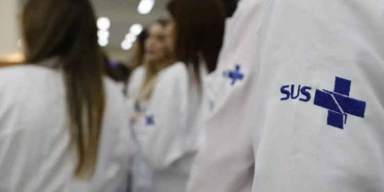 Profissionais de saúde vestindo jalecos do SUS durante atendimento hospitalar.