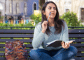 Jovem adulta pensando em parque enquanto escreve em caderno.