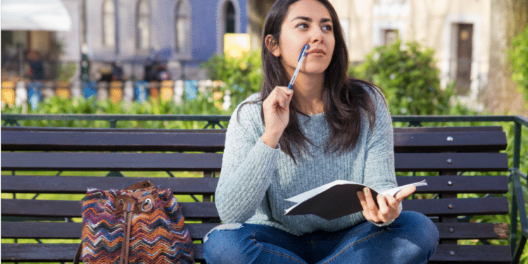 Jovem adulta pensando em parque enquanto escreve em caderno.