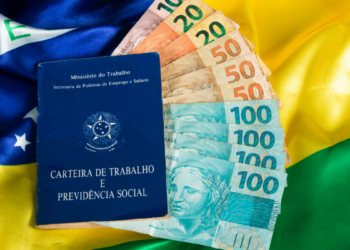 Carteira de trabalho e notas de real sobre bandeira do Brasil.