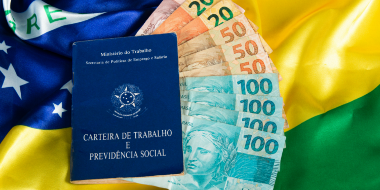 Carteira de trabalho e notas de real sobre bandeira do Brasil.