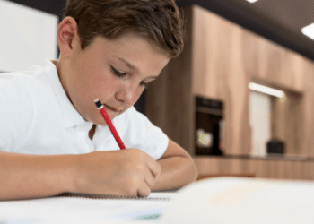 Estudante concentrado escrevendo em caderno durante aula escolar.