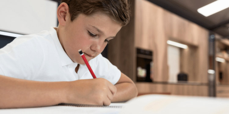 Estudante concentrado escrevendo em caderno durante aula escolar.