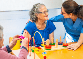Terapeuta ocupacional estimulando idosas com jogos cognitivos em ambiente acolhedor.