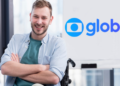 Jovem cadeirante sorridente em ambiente corporativo com logotipo da Globo ao fundo.