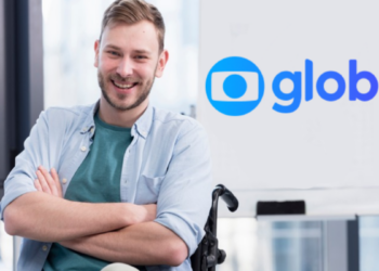 Jovem cadeirante sorridente em ambiente corporativo com logotipo da Globo ao fundo.