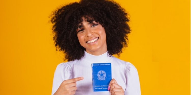 Jovem sorridente exibe carteira de trabalho brasileira em fundo amarelo.