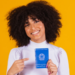 Jovem sorridente exibe carteira de trabalho brasileira em fundo amarelo.
