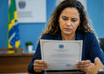 Imagem ilustrativa de servidora analisando com desconfiança um certificado impresso em ambiente de repartição pública, cena ligada ao alerta sobre documentos falsos vendidos em nome da Anvisa.