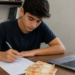Jovem estagiário faz cálculos ao lado de notebook e dinheiro, representando contribuição ao INSS a partir dos 16 anos.