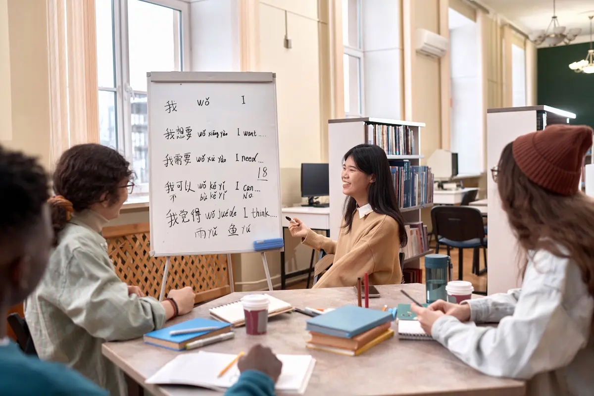 Pessoa estudando japonês em sala de aula com quadro de escrita japonesa ao fundo.