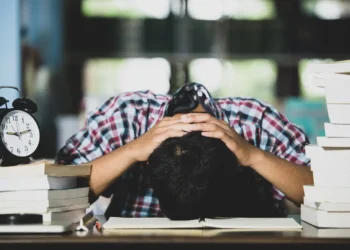 Estudante demonstra cansaço diante de livros e despertador durante uma rotina intensa de estudos.