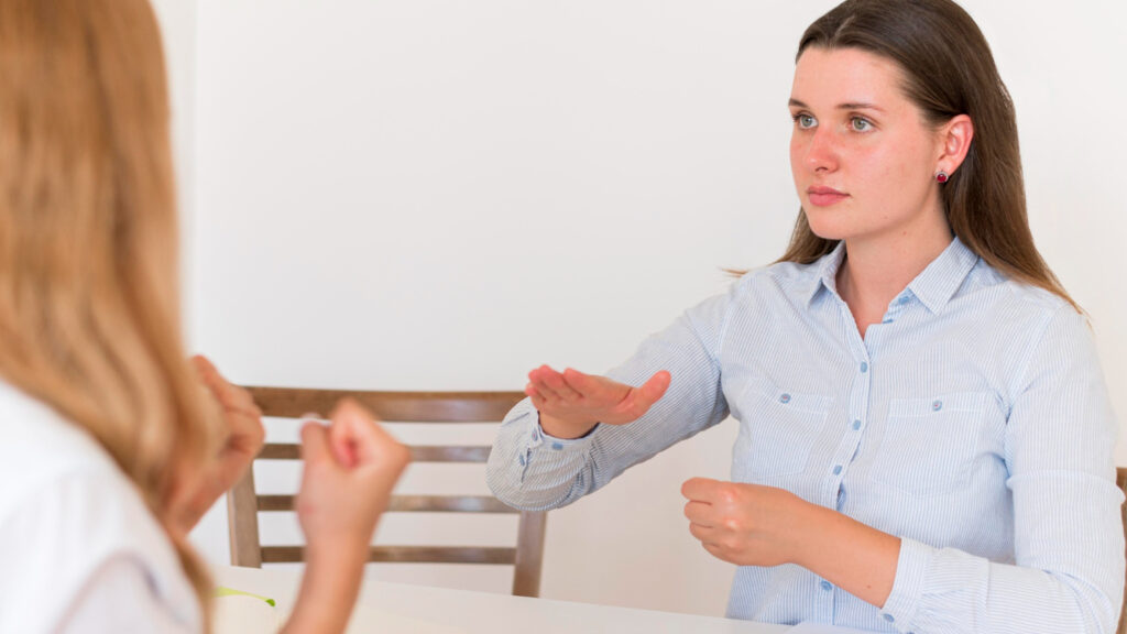 Imagem ilustrativa de duas mulheres conversando em Libras frente a frente durante atendimento, em referência às áreas em que o intérprete de Libras pode atuar