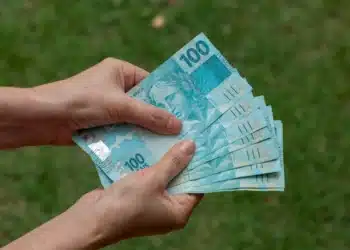 Mãos segurando cédulas de real representando o auxílio financeiro da Bolsa Permanência do ProUni.