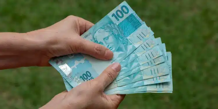 Mãos segurando cédulas de real representando o auxílio financeiro da Bolsa Permanência do ProUni.
