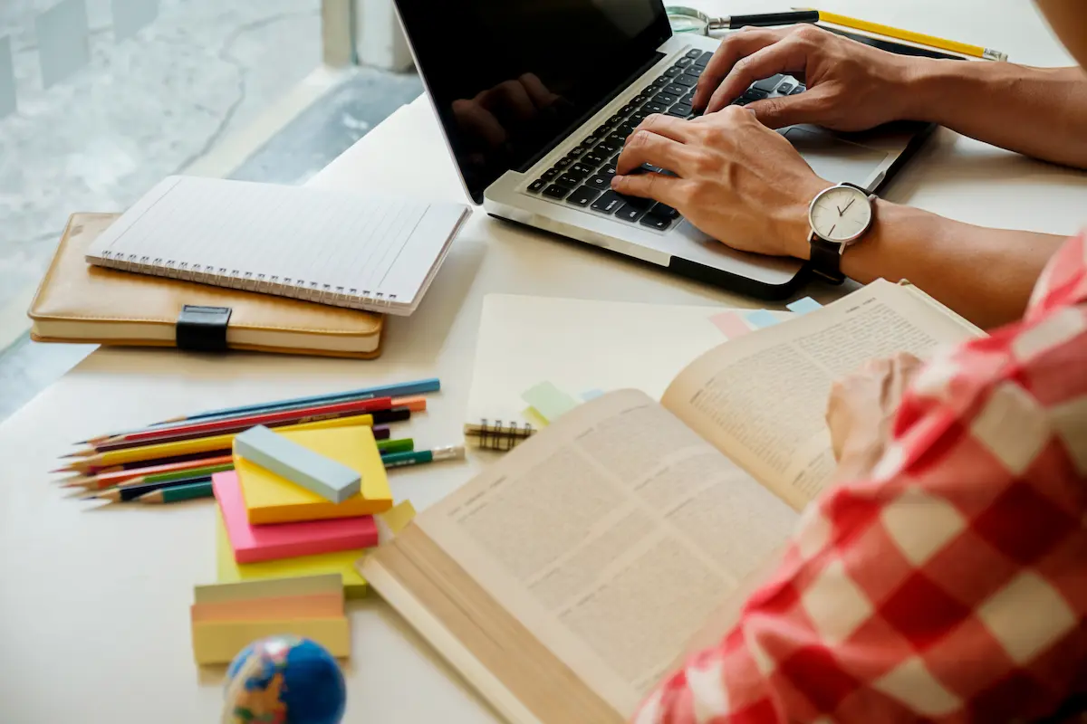 Pessoa estuda com livros, caderno e notebook antes da publicação de um edital de concurso público.