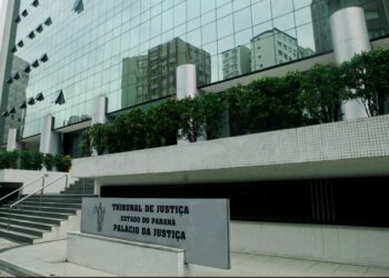 Fachada envidraçada do Palácio da Justiça, sede do Tribunal de Justiça do Paraná, com a placa de identificação em primeiro plano.