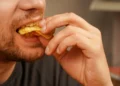 Homem comendo alimento crocante, ilustrando dúvida sobre a grafia de “crocante” ou “cocrante”.