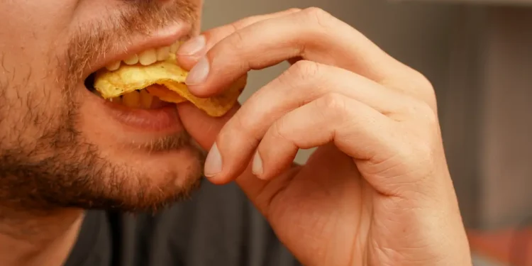 Homem comendo alimento crocante, ilustrando dúvida sobre a grafia de “crocante” ou “cocrante”.
