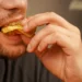 Homem comendo alimento crocante, ilustrando dúvida sobre a grafia de “crocante” ou “cocrante”.