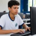 Jovem estudante participa de aula de informática básica em sala equipada com computadores.