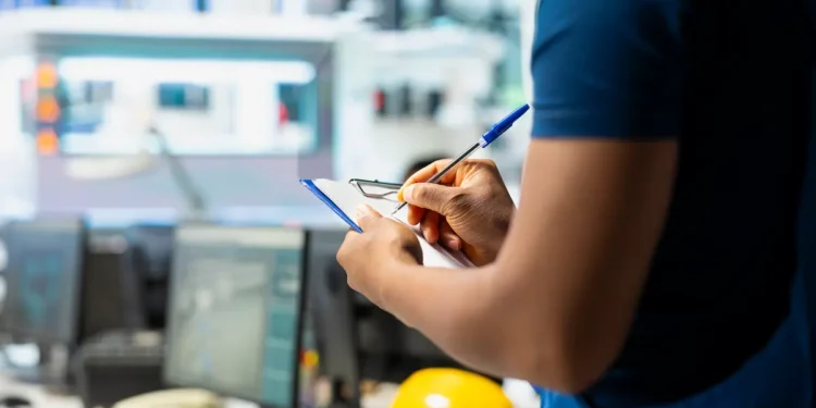 Profissional de curso técnico analisando documentos em ambiente industrial com capacete de segurança ao fundo.
