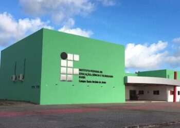 Fachada verde de um campus do Instituto Federal da Bahia, com bandeiras do Brasil e do estado hasteadas na entrada, em referência às unidades que recebem as vagas.
