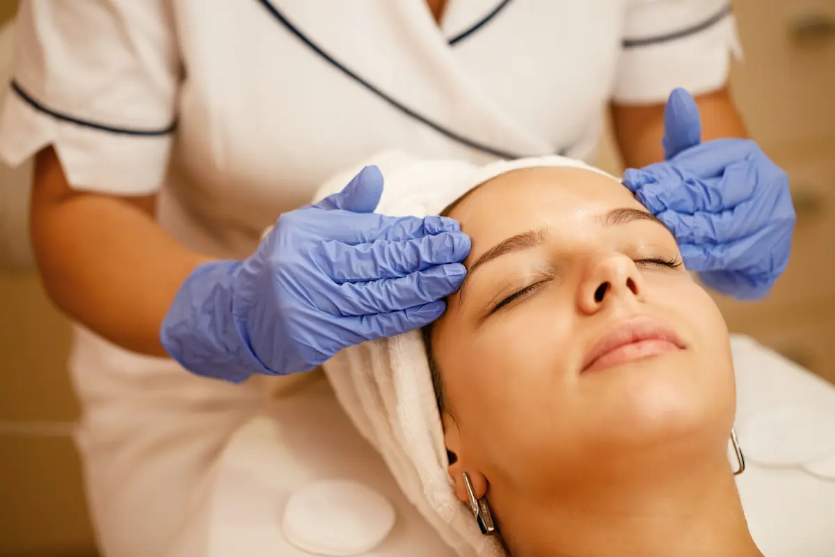 Profissional de estética realizando procedimento facial em cliente durante atendimento técnico especializado.