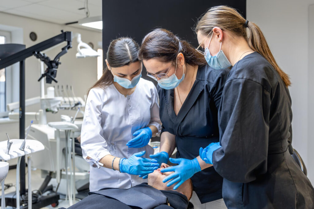 Imagem ilustrativa de equipe de odontologia atendendo um paciente na cadeira do consultório, em referência às atividades exclusivas do cirurgião-dentista diante dos demais profissionais