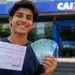 Estudante segurando documento e notas de real em frente a uma agência da Caixa, representando o desconto na dívida do Fies pelo programa Desenrola Adimplentes.