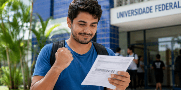 Imagem ilustrativa de jovem comemorando ao ler um boleto em frente a uma universidade federal, representando o estudante diante das novas condições de pagamento