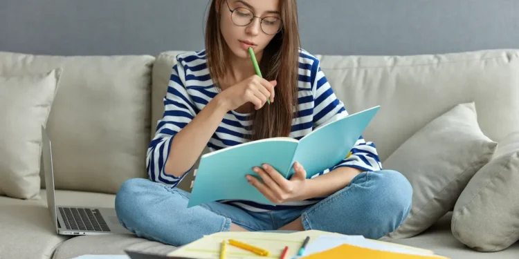 Estudante revisa conteúdos em casa com caderno e notebook durante rotina de estudos.