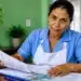Trabalhadora doméstica analisa documentos relacionados ao vínculo empregatício em ambiente residencial, representando os direitos trabalhistas garantidos à categoria.