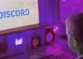 Imagem ilustrativa de monitor exibindo a marca do Discord em um setup de computador com iluminação colorida, cena ligada ao uso da plataforma de comunicação.