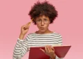 Mulher estudando português com livro e caneta enquanto reflete sobre o uso correto da expressão “Eu vi ele”.