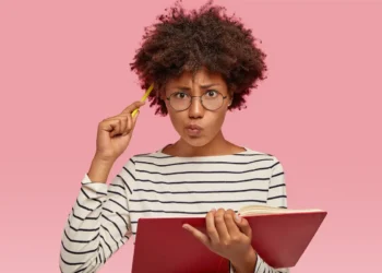 Mulher estudando português com livro e caneta enquanto reflete sobre o uso correto da expressão “Eu vi ele”.