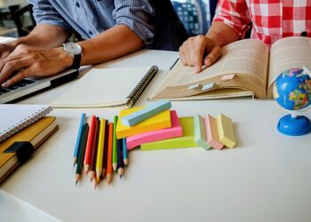 Imagem ilustrativa de mesa de estudos com notebook, livro aberto, cadernos, lápis de cor e globo terrestre, em referência ao levantamento sobre o desempenho de alunos que concluem o ensino médio