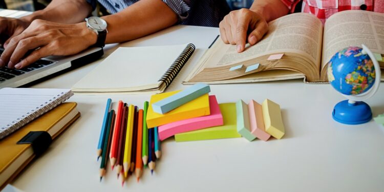 Imagem ilustrativa de mesa de estudos com notebook, livro aberto, cadernos, lápis de cor e globo terrestre, em referência ao levantamento sobre o desempenho de alunos que concluem o ensino médio