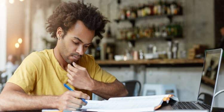 Imagem ilustrativa de estudante concentrado anotando em um caderno ao lado de livro aberto e notebook, cena ligada à organização dos estudos na reta final do Enem 2026.