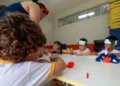 Crianças participam de atividade artística em sala de aula com acompanhamento de educadora.