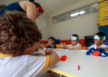 Crianças participam de atividade artística em sala de aula com acompanhamento de educadora.