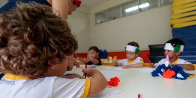 Crianças participam de atividade artística em sala de aula com acompanhamento de educadora.