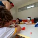 Crianças participam de atividade artística em sala de aula com acompanhamento de educadora.